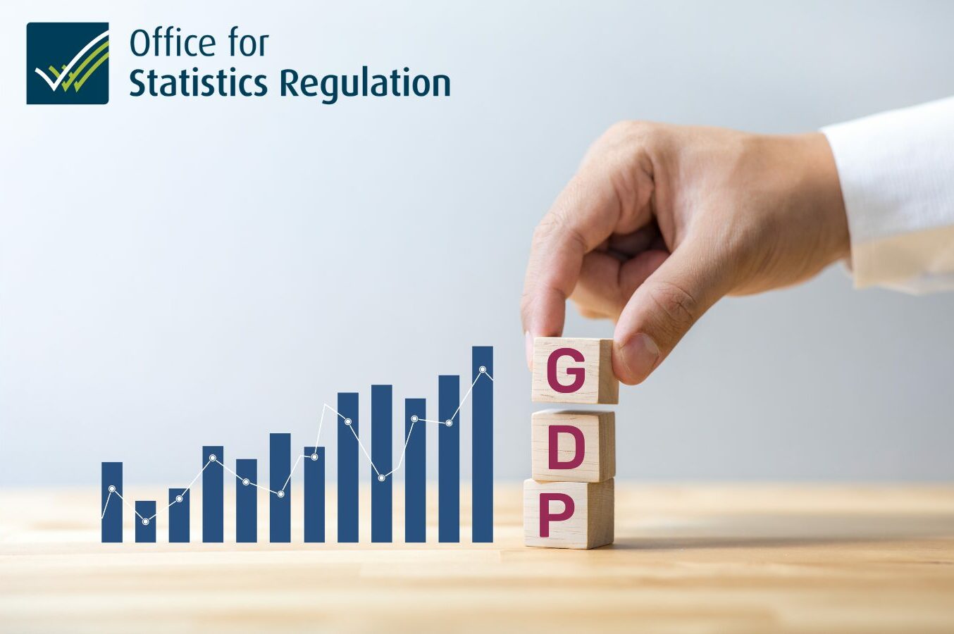 A hand placing three blocks on a table with the letters "GDP" next to a bar chart