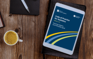 A tablet screen resting on a desk next to a cup of coffee - the tablet is displaying the Code of Practice for Statistics edition 3.0