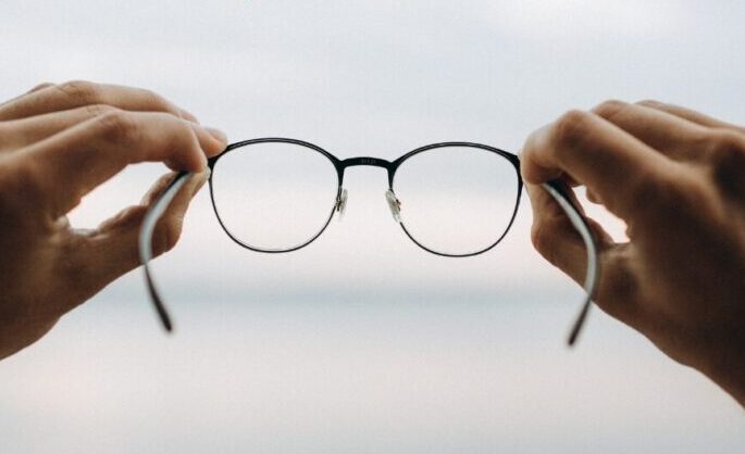 a pair of hands holding a pair of glasses in front of the horizon