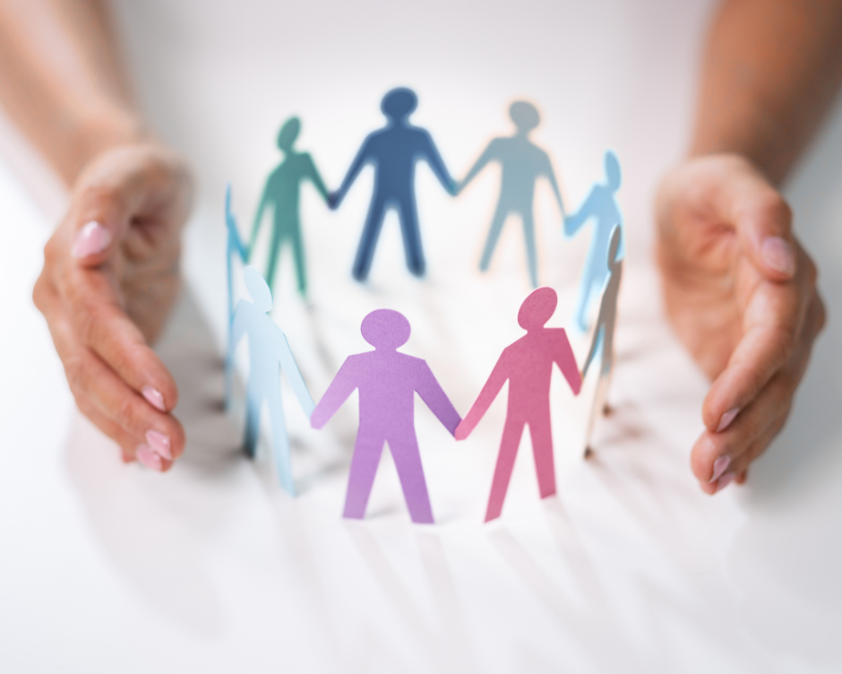 two hands protecting a ring of paper cutout people holding hands